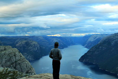 Man standing on rock by lake against sky