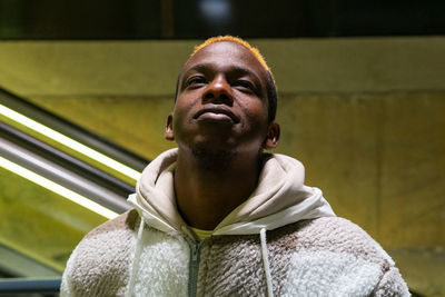 Thoughtful stylish african american male with short dyed hair going down on escalator near shabby stone wall in metro looking up