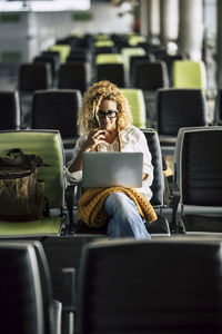 Smiling woman using laptop while sitting at airport