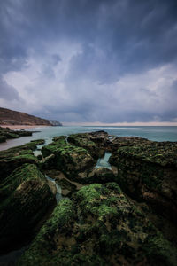 Scenic view of rock formations by sea against cloudy sky