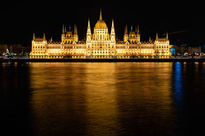 Hungarian parliament building by danube river against sky at night