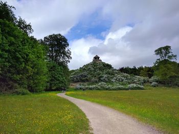 Road passing through field against cloudy sky