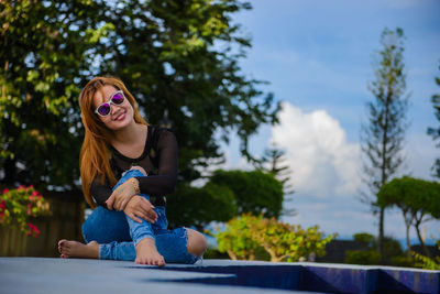 Smiling young woman sitting against trees