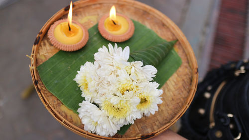 Cropped hand of woman holding flower and diya in plate