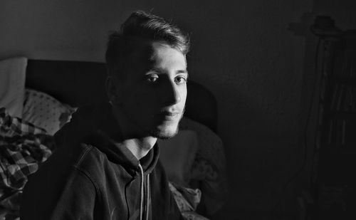 Portrait of young man sitting on bed at home