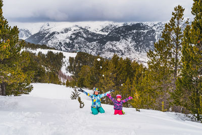 Mother and daughter sitting on a snow and throwing snow up. winter ski holidays in andorra