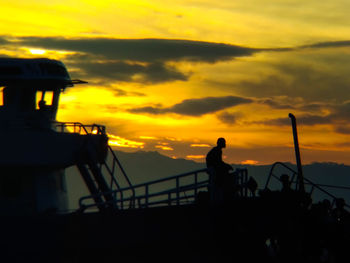 Silhouette man by sea against sky during sunset