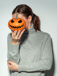 Woman covering face with pumpkin against gray background