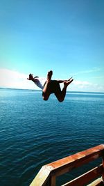 Full length of man jumping in sea against blue sky
