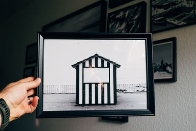 Close-up of person holding photo of beach house in front of wall