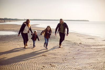 Family in a leather jacket run along the beach with their dog in autumn