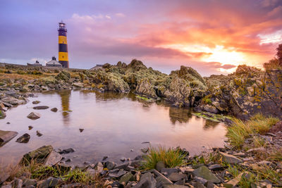 Lighthouse amidst rocks against sky during sunset