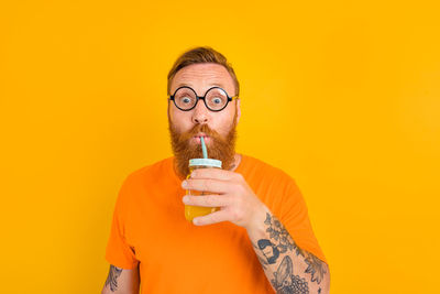 Portrait of man holding yellow glass against orange background