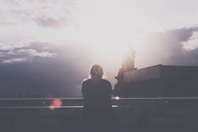 Woman standing by railing in city against sky