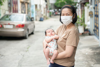 Asian mother wearing surgical face mask holding her baby, covid-19 concept