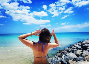 Rear view of woman standing at beach against sky