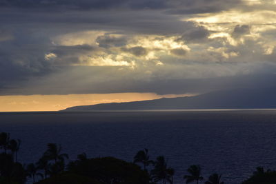 Sunbeams streaming from cloudy sky over sea during sunset