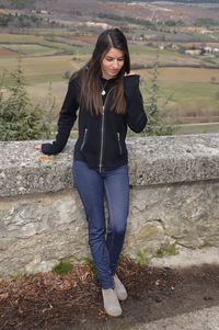 Woman standing by retaining wall against landscape