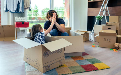 Brother and sister high-fiving while sitting in cardboard box in new house