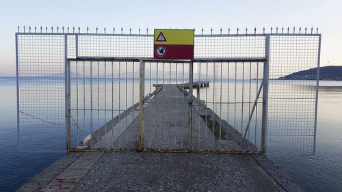 Road sign by railing against sky