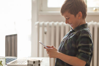 Cheerful boy laughing to a text message he has received over cell phone at home.