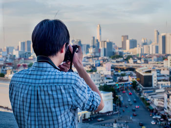 Rear view of man photographing cityscape against sky