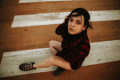 Portrait of young woman sitting on zebra crossing