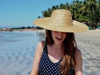 Young woman with hat on beach against sky