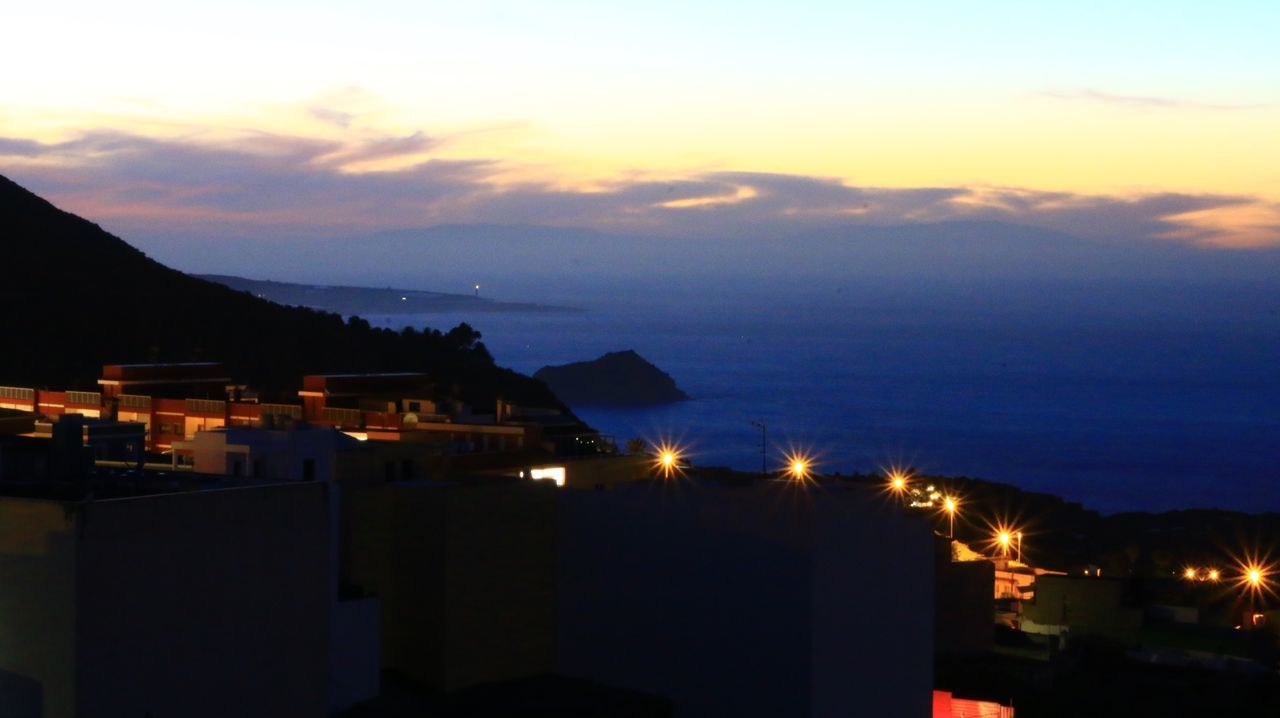 HIGH ANGLE VIEW OF ILLUMINATED BUILDINGS IN CITY AGAINST SKY AT SUNSET