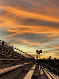 Bleachers at a sports field against sky during sunset with palm trees