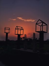 Silhouette cranes at playground against sky during sunset