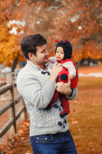 Father carrying cute daughter while standing in park during autumn