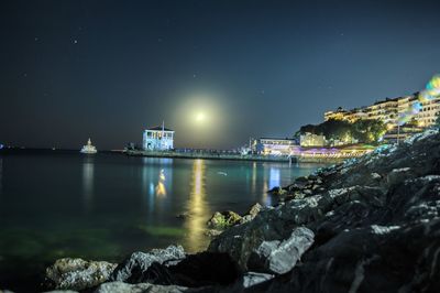 Illuminated rocks by sea against sky at night