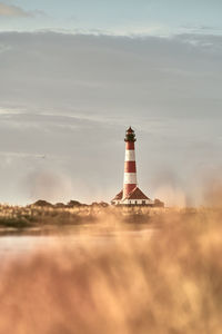 Lighthouse by sea against sky during sunset