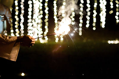 Cropped hand holding lit sparkler at night