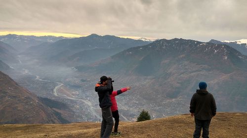 Rear view of people standing on mountain against sky