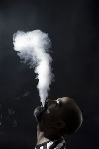 Profile view of bald man smoking against black background