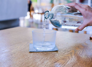 Midsection of person pouring drink in glass on table