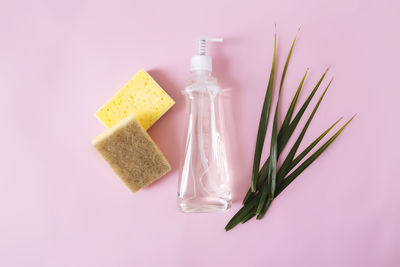 Flat lay with palm leaf, soap dropper, dishwashing liquid, dish soap, washcloth on pink background