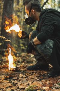Man wearing mask while holding fire in forest