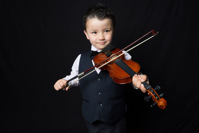 Portrait of boy playing violin against black background