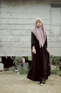 Portrait of young woman standing against wall