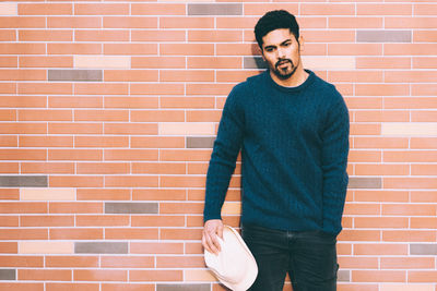 Portrait of young man standing against brick wall