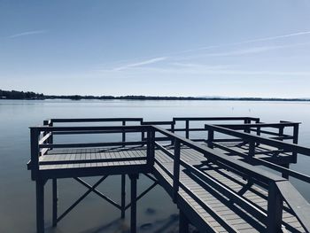 Empty bench by pier on lake against sky