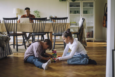 Siblings playing jenga while sitting on floor at home