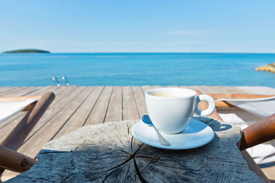 Coffee cup on table by sea against sky