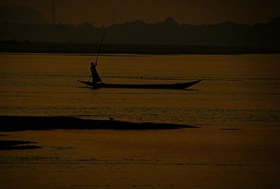 Silhouette man in boat against sky during sunset