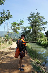 Portrait of man wearing life jacket while standing on dirt road against clear blue sky