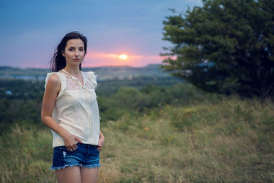 Young woman standing on field against sky during sunset