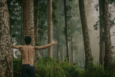 Rear view of shirtless man standing in forest